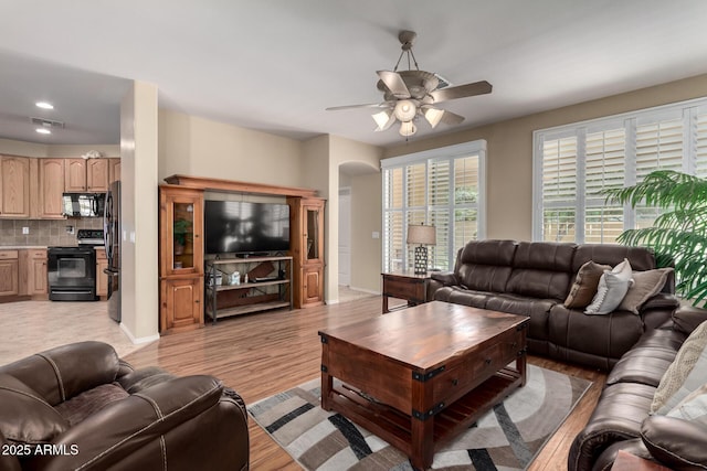 living area featuring a ceiling fan, baseboards, visible vents, arched walkways, and light wood-type flooring