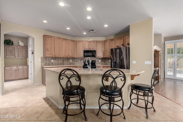 kitchen with visible vents, a center island with sink, decorative backsplash, black appliances, and a sink