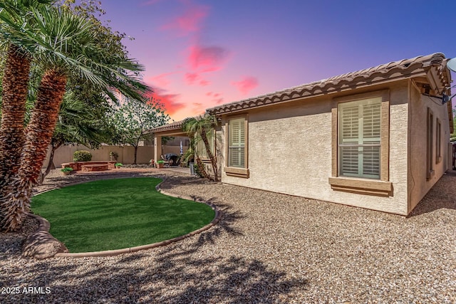 rear view of property featuring a tiled roof, stucco siding, a lawn, a fenced backyard, and a patio area