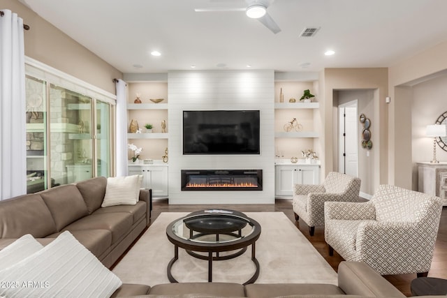 living room featuring ceiling fan, a large fireplace, wood-type flooring, and built in features