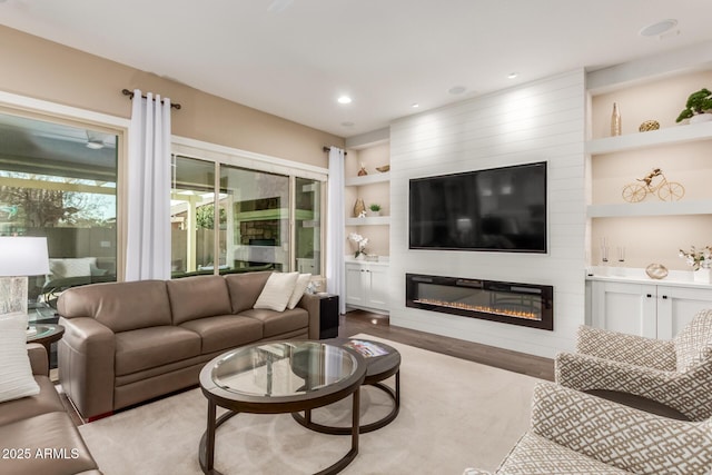 living room with built in shelves, a large fireplace, and light wood-type flooring