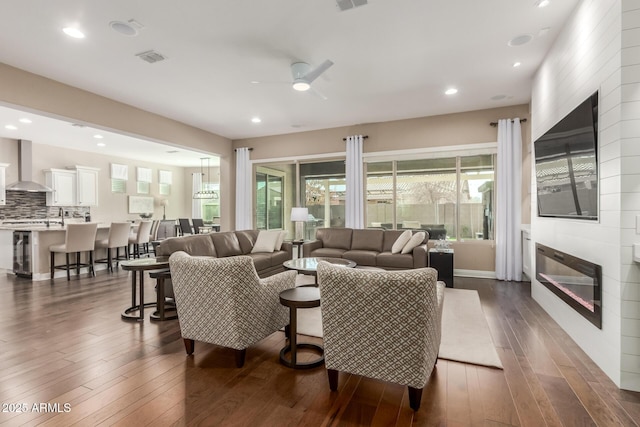 living room with dark hardwood / wood-style flooring, sink, a large fireplace, and ceiling fan