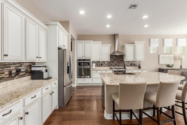 kitchen featuring light stone countertops, appliances with stainless steel finishes, wall chimney range hood, and white cabinets