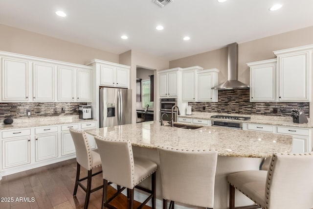 kitchen featuring white cabinetry, sink, a kitchen island with sink, stainless steel appliances, and wall chimney range hood