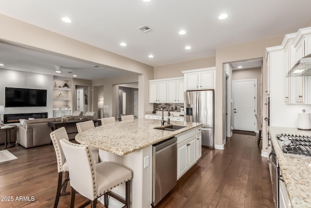 kitchen featuring stainless steel appliances, a kitchen island with sink, light stone counters, and a kitchen breakfast bar