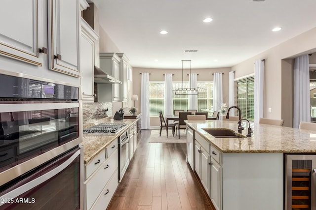 kitchen featuring pendant lighting, sink, wine cooler, stainless steel appliances, and a center island with sink