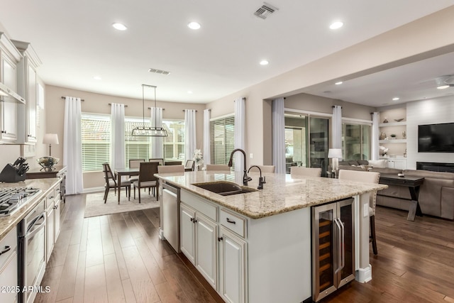 kitchen featuring sink, hanging light fixtures, a center island with sink, stainless steel appliances, and beverage cooler