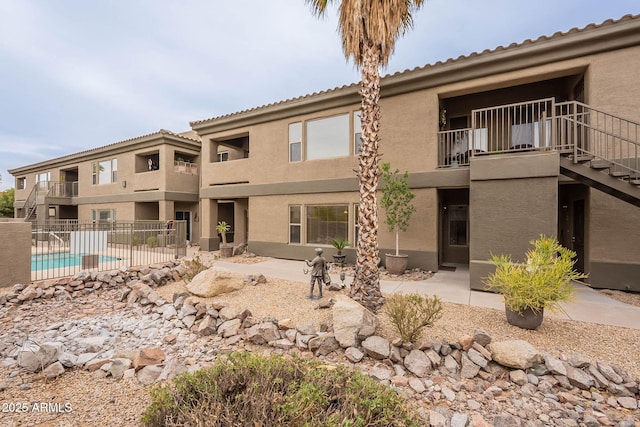 rear view of property featuring a fenced in pool, a patio, and a balcony