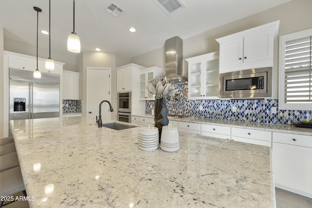 kitchen featuring pendant lighting, range hood, white cabinetry, sink, and built in appliances