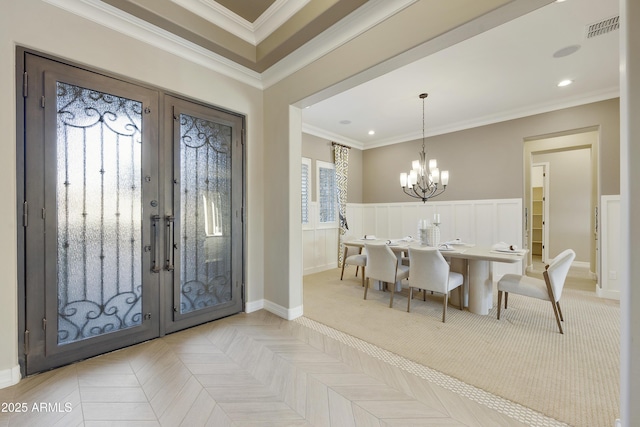 entrance foyer with an inviting chandelier, ornamental molding, french doors, and light parquet flooring