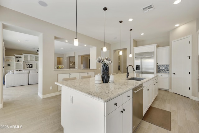 kitchen featuring sink, a kitchen island with sink, white cabinetry, stainless steel appliances, and decorative light fixtures