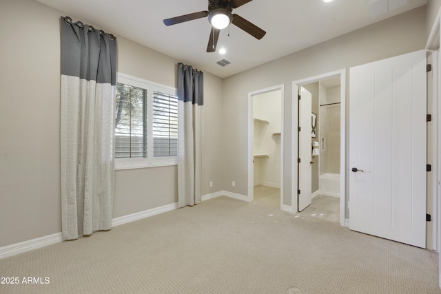 unfurnished bedroom featuring ensuite bath, a walk in closet, light colored carpet, and ceiling fan