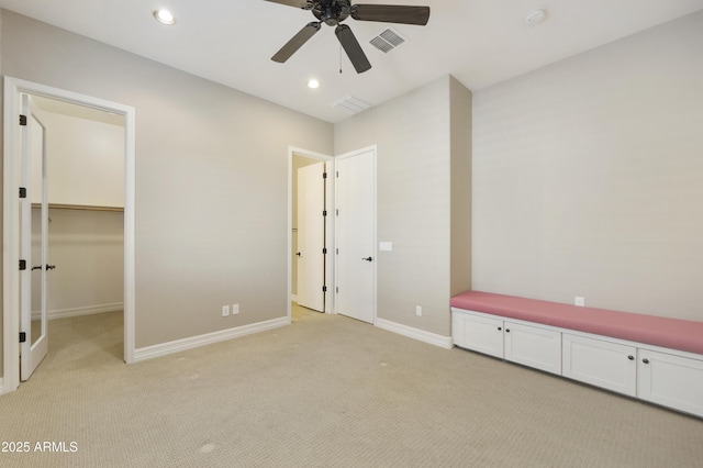 unfurnished bedroom featuring a walk in closet, light colored carpet, and ceiling fan