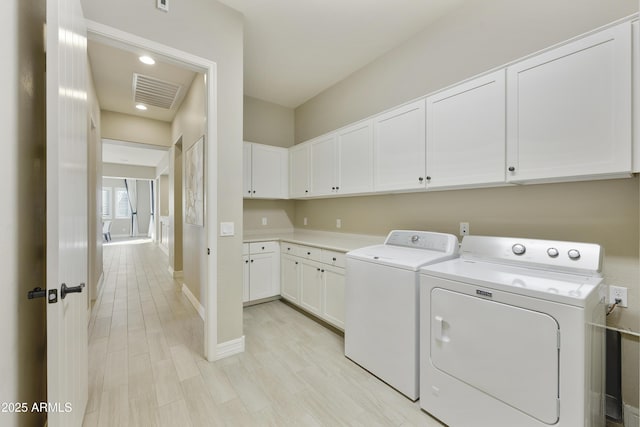 clothes washing area featuring cabinets, washing machine and dryer, and light hardwood / wood-style flooring