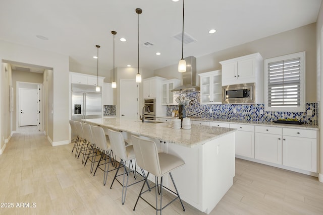 kitchen with a spacious island, built in appliances, decorative light fixtures, range hood, and white cabinets