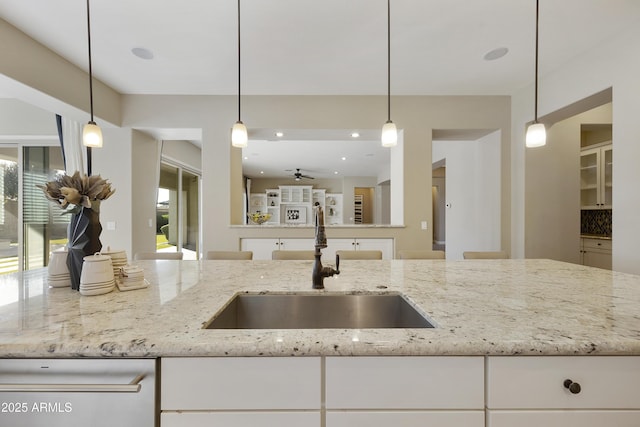 kitchen with light stone countertops, sink, hanging light fixtures, and white cabinets