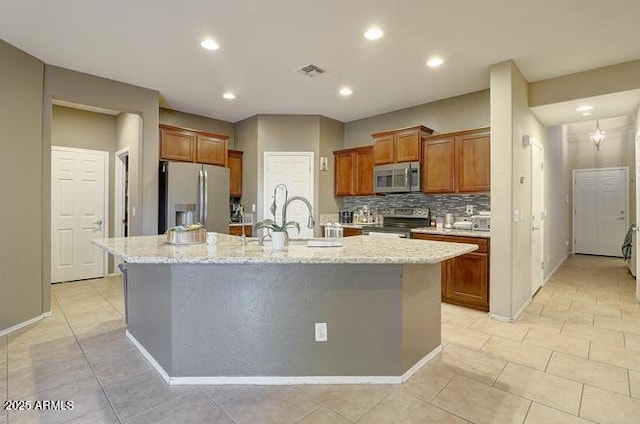 9009 S 57th Dr, Laveen, AZ 85339 - kitchen featuring backsplash, a center island with sink, brown cabinetry, stainless steel appliances, and visible vents