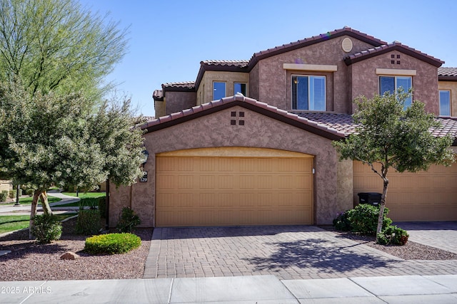 mediterranean / spanish-style home with a tile roof, decorative driveway, a garage, and stucco siding