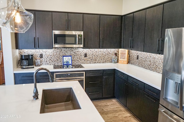 kitchen with a sink, decorative backsplash, light countertops, stainless steel appliances, and light wood-style floors