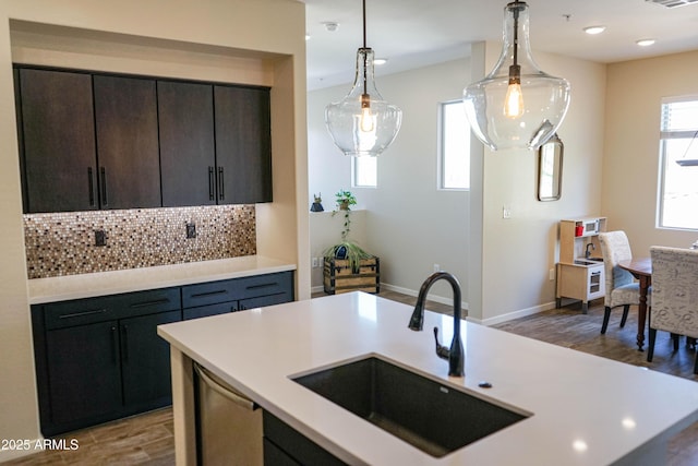 kitchen featuring a sink, wood finished floors, light countertops, decorative backsplash, and hanging light fixtures