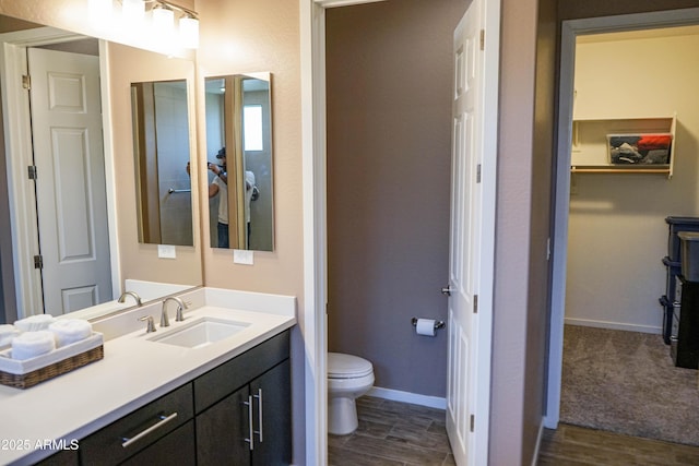 bathroom with toilet, vanity, baseboards, and wood finished floors