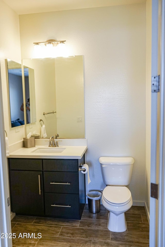 bathroom with baseboards, toilet, vanity, and wood finish floors