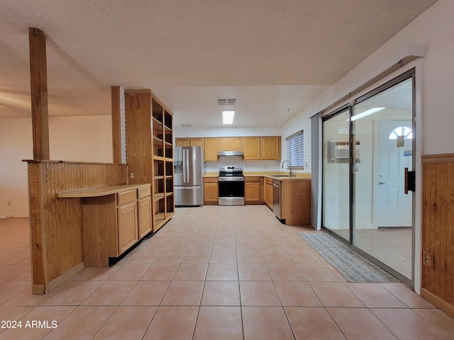 kitchen with kitchen peninsula, wooden walls, sink, light tile patterned flooring, and appliances with stainless steel finishes