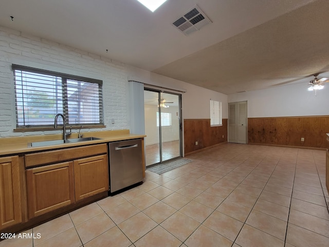 kitchen with brick wall, stainless steel dishwasher, sink, and wooden walls