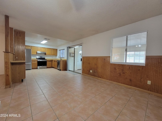 kitchen featuring a textured ceiling, stainless steel appliances, wood walls, and light tile patterned floors