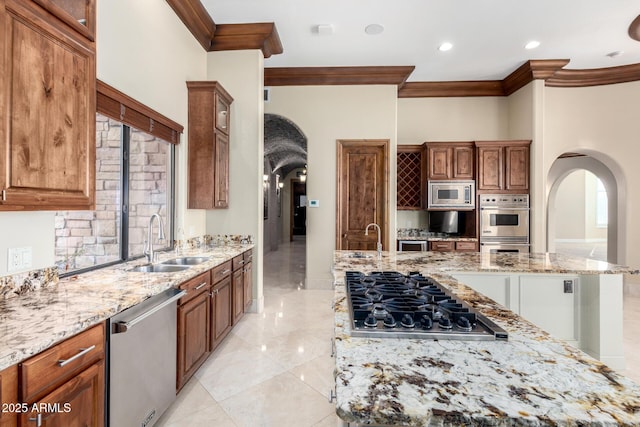 kitchen with stainless steel appliances, light stone countertops, sink, and a center island with sink