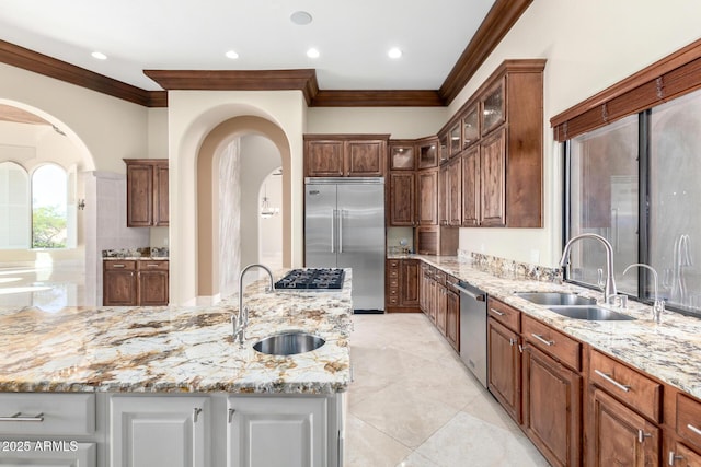 kitchen with a kitchen island with sink, appliances with stainless steel finishes, light stone countertops, and sink