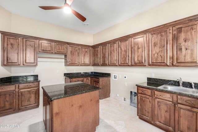 kitchen featuring ceiling fan, sink, a kitchen island, and dark stone countertops