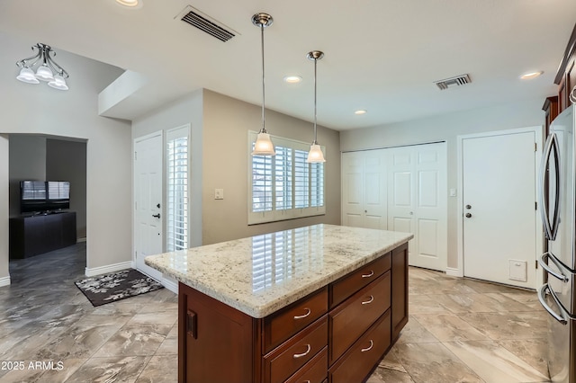 kitchen with light stone counters, decorative light fixtures, a center island, and stainless steel refrigerator