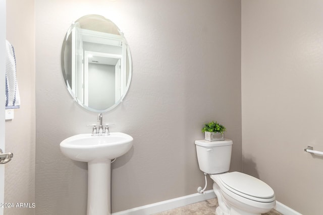 half bath featuring baseboards, toilet, and a sink