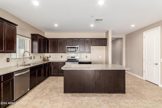 kitchen featuring light stone counters, a sink, a center island, stainless steel appliances, and visible vents