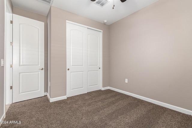 unfurnished bedroom featuring a closet, dark colored carpet, baseboards, visible vents, and ceiling fan