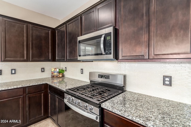 kitchen with light stone counters, appliances with stainless steel finishes, backsplash, and dark brown cabinets