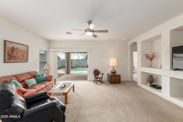 carpeted living room with a ceiling fan and arched walkways