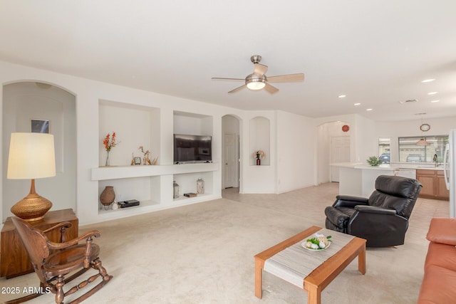 living area featuring arched walkways, a ceiling fan, light carpet, and recessed lighting