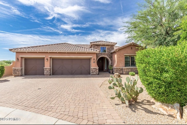 mediterranean / spanish home featuring an attached garage, stone siding, and stucco siding