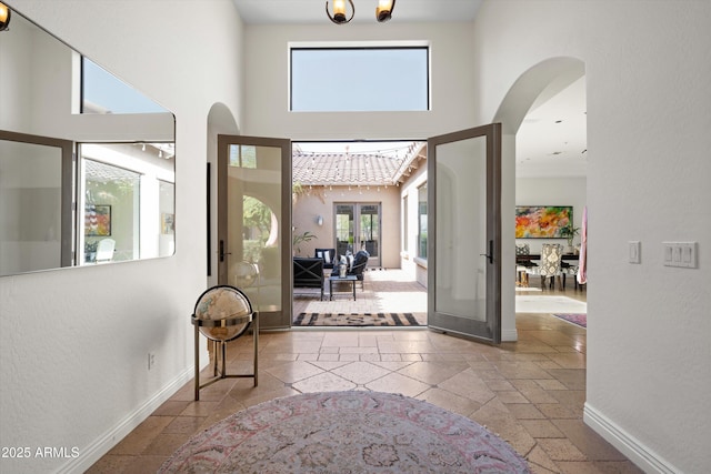 foyer entrance featuring arched walkways, french doors, stone tile floors, a towering ceiling, and baseboards