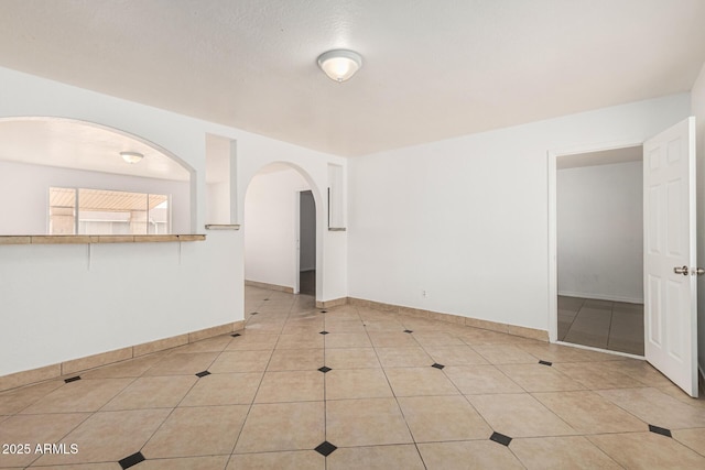 empty room featuring light tile patterned floors, arched walkways, and baseboards