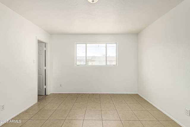 unfurnished room with baseboards, a textured ceiling, and light tile patterned flooring