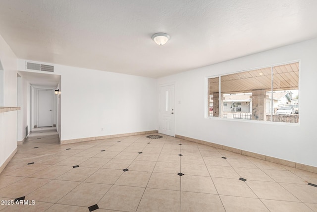 spare room featuring baseboards, visible vents, a textured ceiling, and light tile patterned flooring