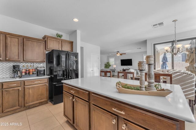 kitchen featuring backsplash, black fridge with ice dispenser, ceiling fan with notable chandelier, light tile patterned floors, and decorative light fixtures