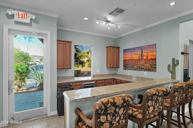 kitchen with a kitchen breakfast bar, kitchen peninsula, light stone countertops, and crown molding