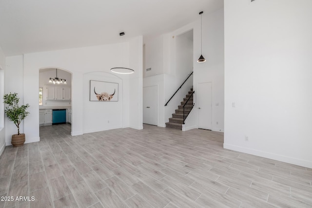 8478 W Grovers Ave, Peoria, AZ 85382 - unfurnished living room with high vaulted ceiling, light wood-type flooring, stairs, arched walkways, and a chandelier