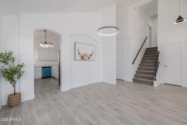 8478 W Grovers Ave, Peoria, AZ 85382 - unfurnished living room featuring light wood finished floors, stairs, a chandelier, a towering ceiling, and arched walkways