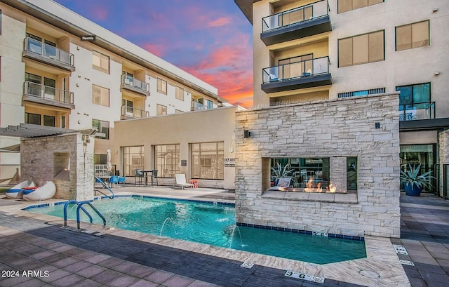 pool at dusk featuring pool water feature and a patio area