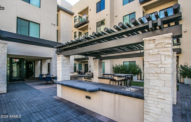 view of patio featuring an outdoor kitchen, a balcony, sink, grilling area, and a pergola